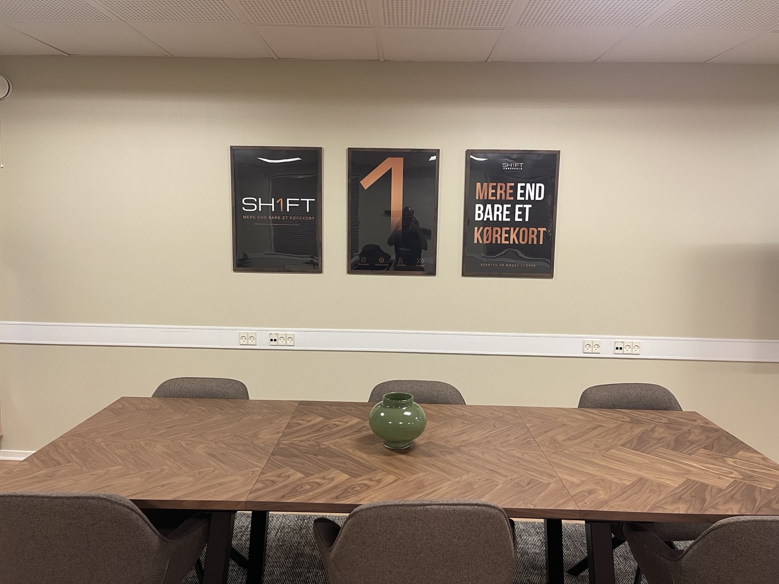 Undervisningsbordet i SH1FTs teorilokale med SH1FT-plakater på væggen